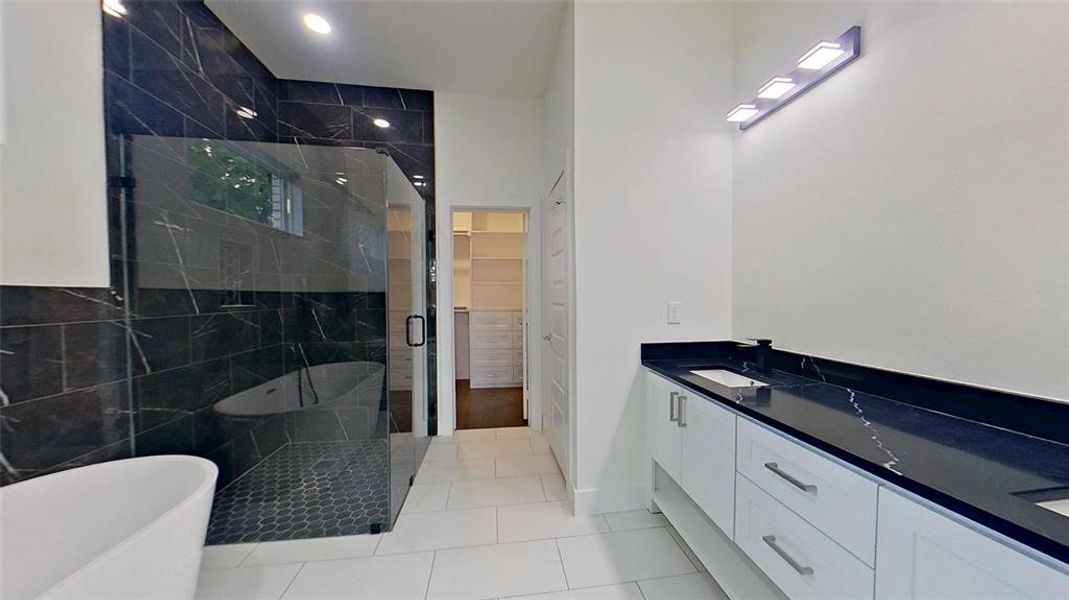 Bathroom featuring double vanity, a freestanding tub, a marble finish shower, light tile patterned floors, and a walk in closet