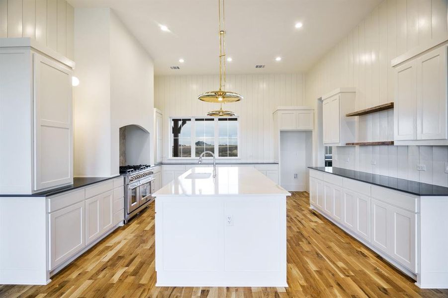 Kitchen with white cabinets, decorative light fixtures, range with two ovens, and light hardwood / wood-style floors