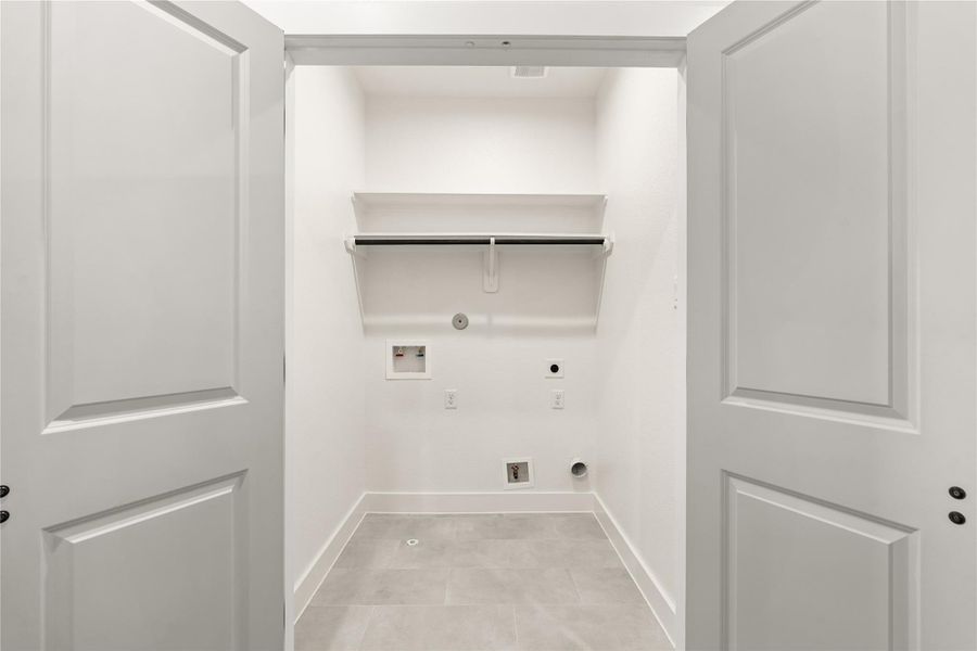 Dedicated laundry room with utility connections, overhead storage, and tile floor Dedicated laundry room with utility connections, overhead storage, and tile floor