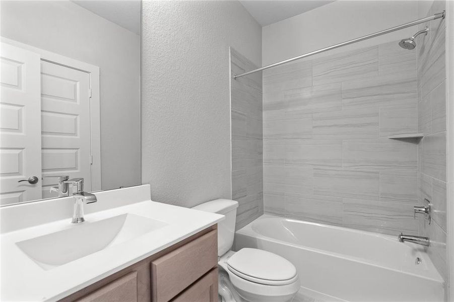 Secondary bath features tile flooring, bath/shower combo with tile surround, stained wood cabinets, beautiful light countertops, mirror, sleek fixtures and modern finishes.