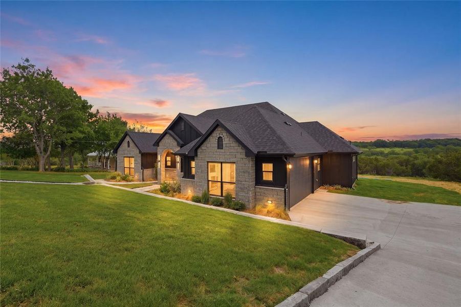 Stone and dark-paneled exterior featuring multiple gables, a dark shingle roof, and a concrete driveway
