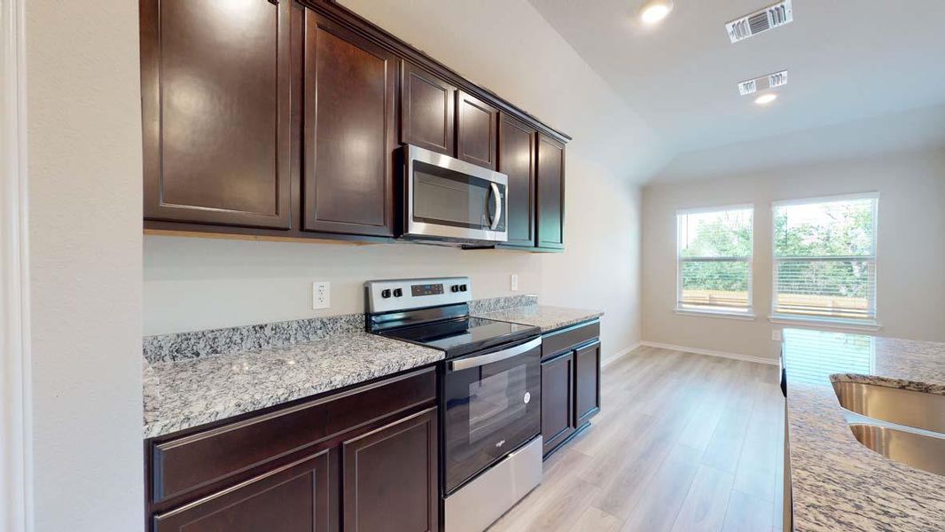 Kitchen area featuring granite countertops, dark wood cabinetry, stainless steel appliances, and wood-finish flooring