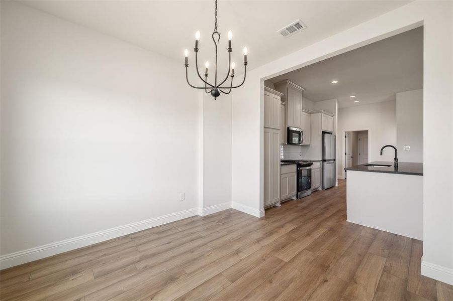 Kitchen with appliances with stainless steel finishes, dark countertops, a chandelier, light wood-type flooring, and recessed lighting