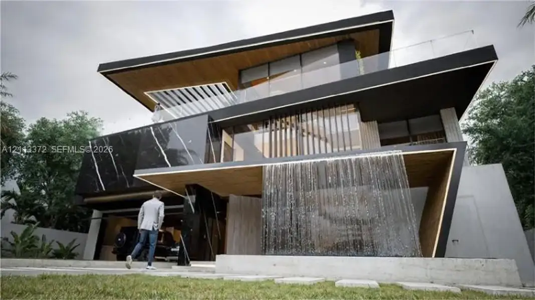 Contemporary architectural exterior featuring a tiered design, integrated water feature, wood-finish soffits, stone cladding with veining, and glass balcony railings