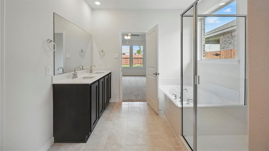 Full bath featuring a bath, double vanity, a shower stall, light tile patterned flooring, and a ceiling fan