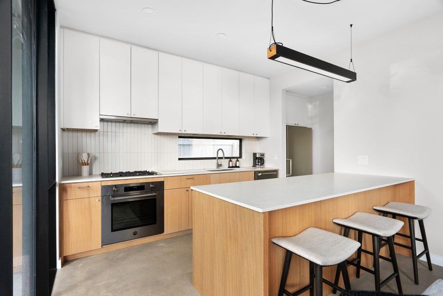 Kitchen with a kitchen bar, a peninsula, light countertops, stainless steel oven, and finished concrete floors Kitchen with a kitchen bar, a peninsula, light countertops, stainless steel oven, and finished concrete floors