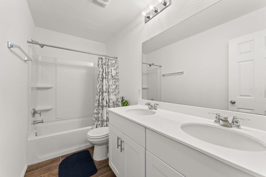 Bathroom with wood tiled floor, double vanity, a sink, and shower / bath combo