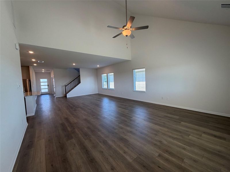 Unfurnished living room with high vaulted ceiling, dark wood-type flooring, a ceiling fan, stairs, and recessed lighting Unfurnished living room with high vaulted ceiling, dark wood-type flooring, a ceiling fan, stairs, and recessed lighting