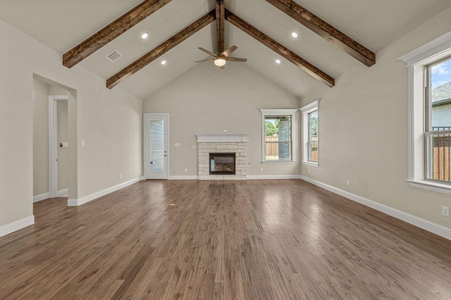 Unfurnished living room featuring a fireplace, plenty of natural light, beamed ceiling, and hardwood / wood-style flooring