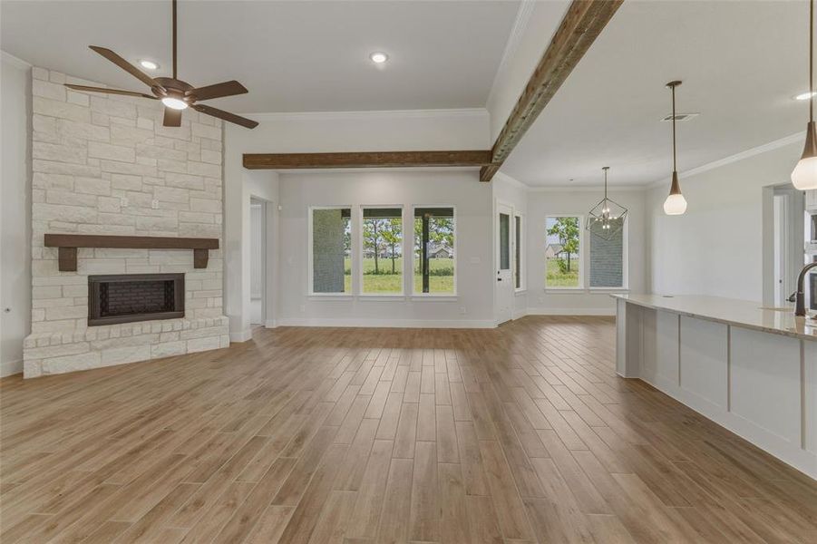 Spacious living area featuring wood-finish flooring, a stone-clad fireplace with a wood mantle, an overhead ceiling fan, and exposed wood beams Spacious living area featuring wood-finish flooring, a stone-clad fireplace with a wood mantle, an overhead ceiling fan, and exposed wood beams