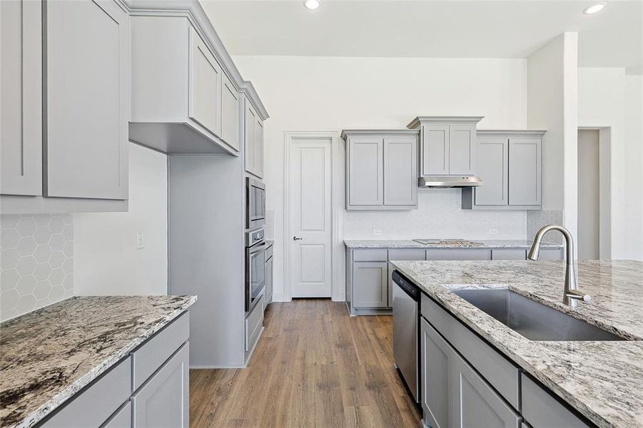 Kitchen featuring light stone countertops, gray cabinets, wood finished floors, decorative backsplash, and recessed lighting