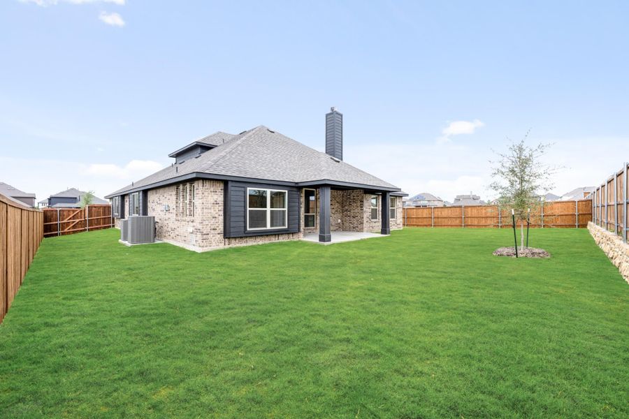Rear view of single-story brick home with chimney, covered patio, and large fenced backyard with green lawn Rear view of single-story brick home with chimney, covered patio, and large fenced backyard with green lawn