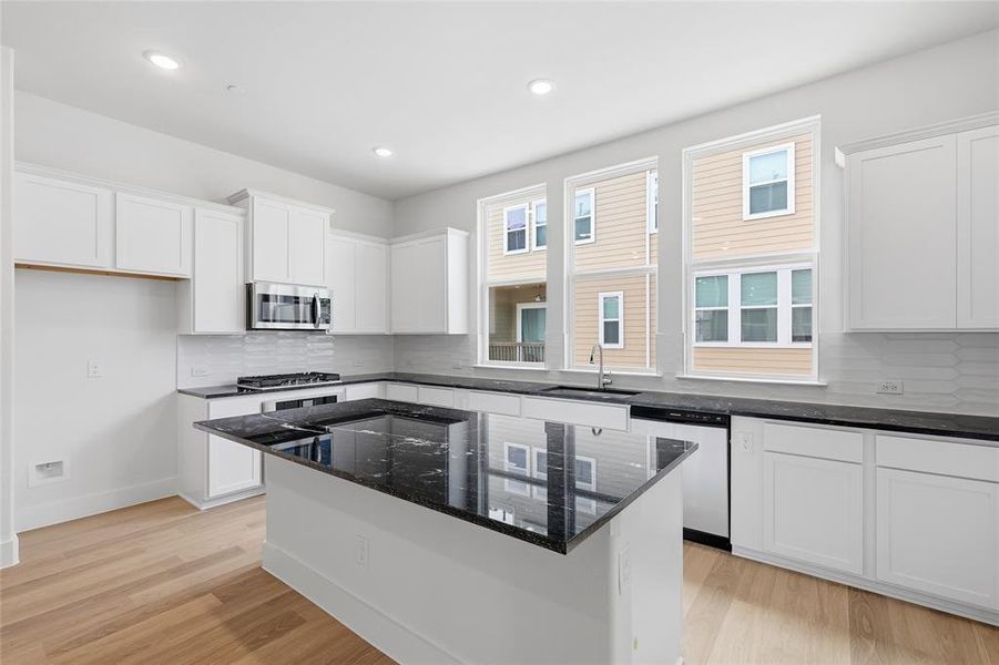 Well-appointed kitchen featuring light wood flooring, white cabinetry, a black island countertop, and a stainless steel microwave