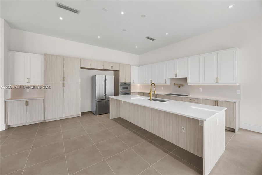 Spacious kitchen featuring an expansive island, stainless steel appliances, integrated cooktop, abundant cabinetry, and tile flooring