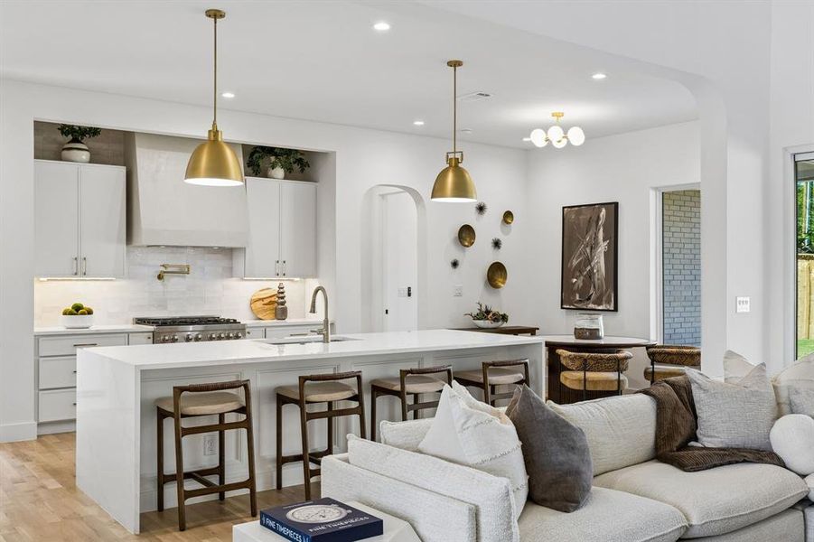 Kitchen with arched walkways, a kitchen breakfast bar, white cabinets, a kitchen island with sink, and light wood-style flooring