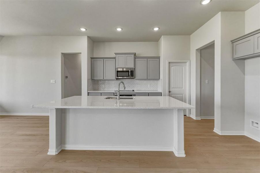 Kitchen island with a light-toned countertop and integrated sink, complemented by light grey cabinetry and a patterned tile backsplash