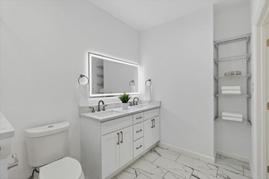 Double vanity featuring white cabinetry, integrated sinks, and a quartz countertop.  Ample shelving for towels and other necessities.