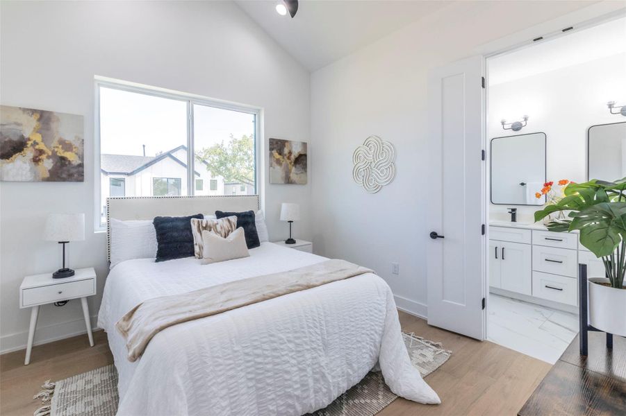Bedroom featuring vaulted ceiling, light wood-style floors, and ensuite bathroom