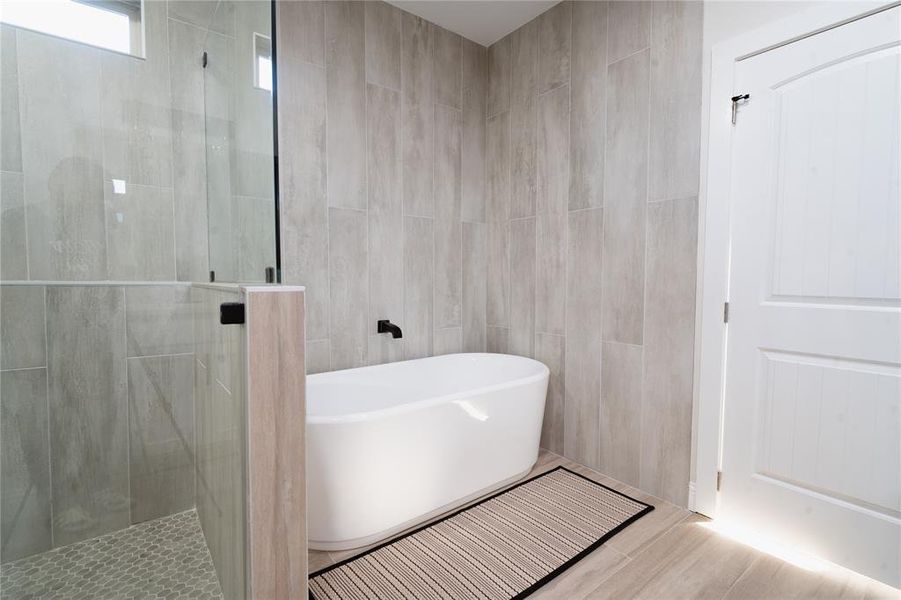 Full bathroom with a stall shower, a soaking tub, wood finished floors, and tile walls