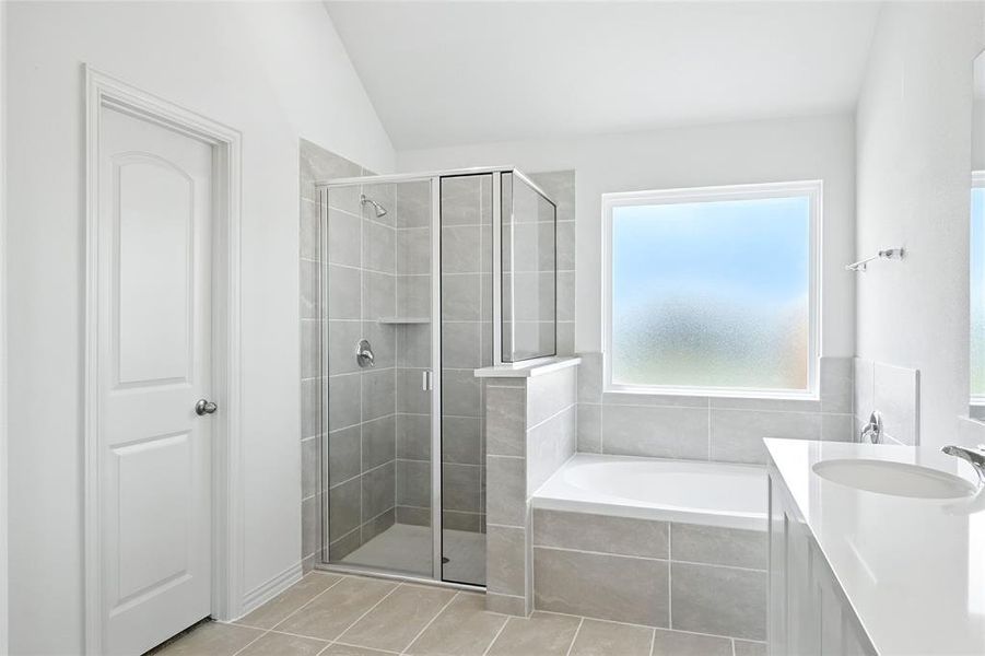 Full bath featuring a bath, a stall shower, vanity, light tile patterned floors, and lofted ceiling Full bath featuring a bath, a stall shower, vanity, light tile patterned floors, and lofted ceiling