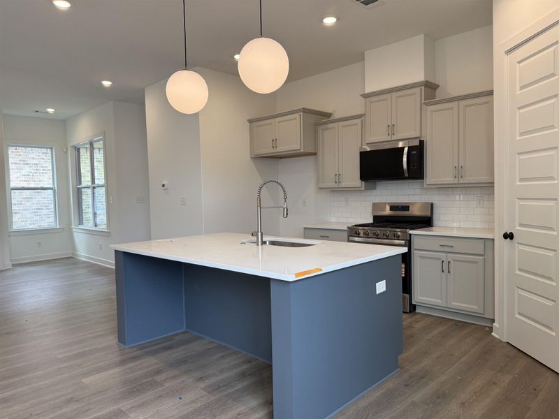 Kitchen featuring a large central island with a white countertop, pendant lighting, stainless steel appliances, light gray cabinetry, and white subway tile backsplash