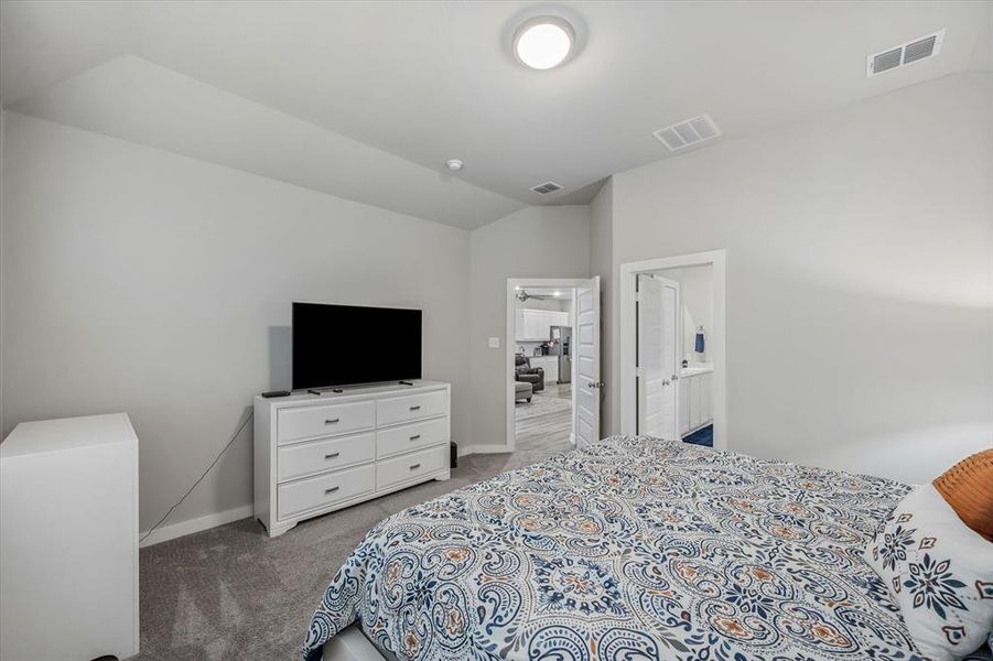 Bedroom featuring carpet, ensuite bathroom, and lofted ceiling