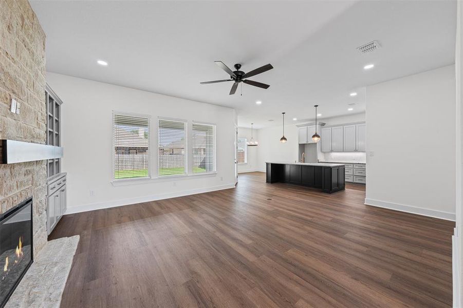 This expansive living area features rich hardwood flooring, a modern fireplace with a stone surround, and large windows offering views of the yard