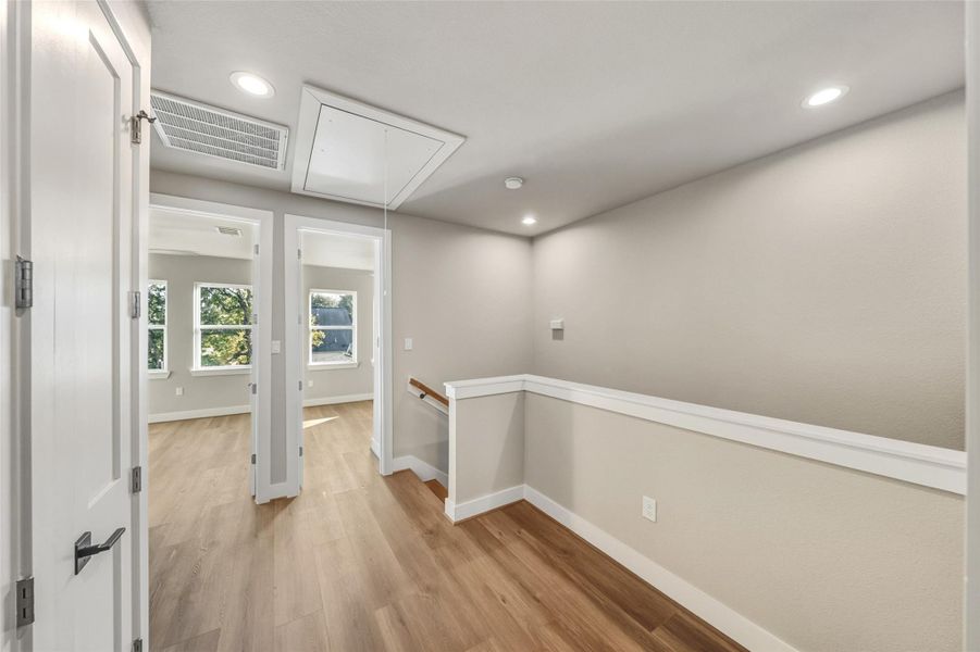 This inviting hallway, bathed in natural light and featuring sleek wood flooring, seamlessly connects to all three bedrooms, offering both style and functionality.