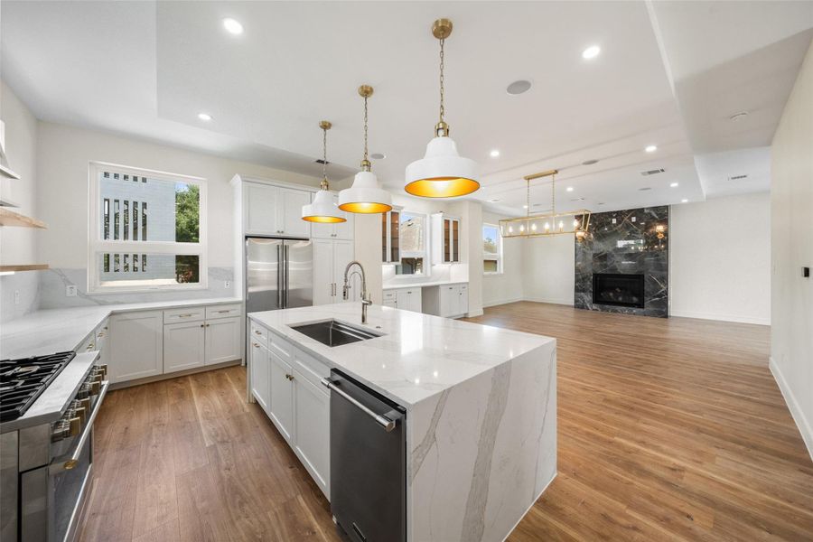 Kitchen features sleek white cabinetry, a large island with a marble countertop, and stainless steel appliances. It opens into a spacious living area with a stylish black marble fireplace, offering a perfect setting for entertaining.