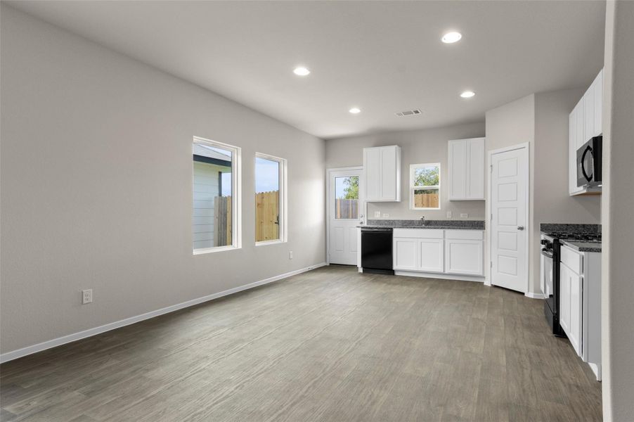 Kitchen featuring black appliances, recessed lighting, wood finished floors, white cabinetry, and dark stone countertops Kitchen featuring black appliances, recessed lighting, wood finished floors, white cabinetry, and dark stone countertops