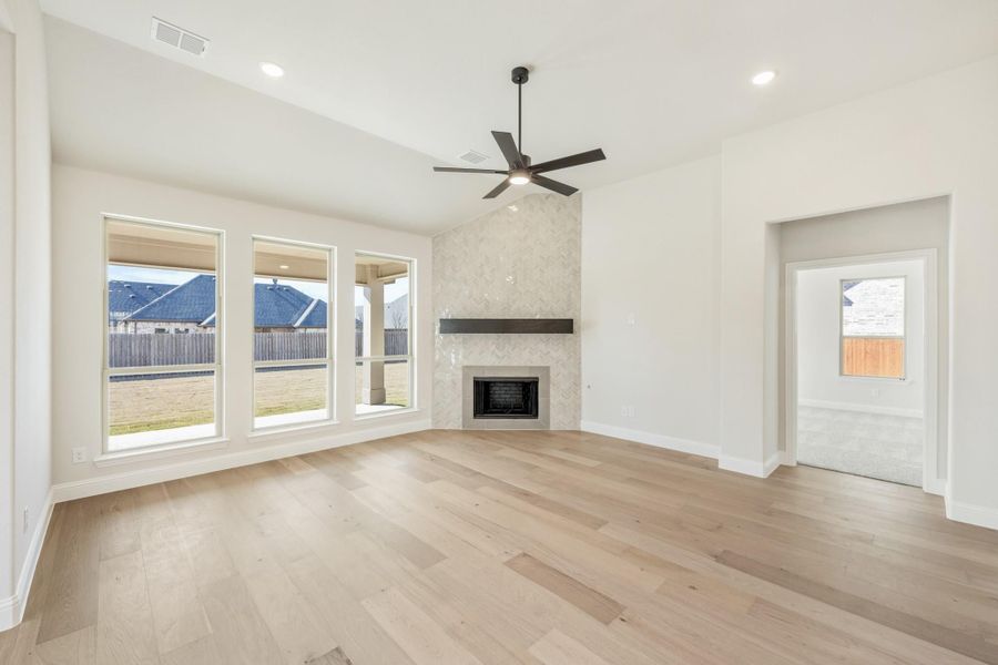 Open living room with hardwood floors, ceiling fan, tile fireplace, and large windows overlooking backyard