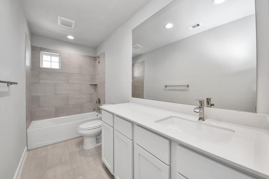 Secondary bath features tile flooring, bath/shower combo with tile surround, light stained wood cabinets, beautiful light countertop. Sample photo of completed home with similar floor plan. Actual colors and selections may vary.