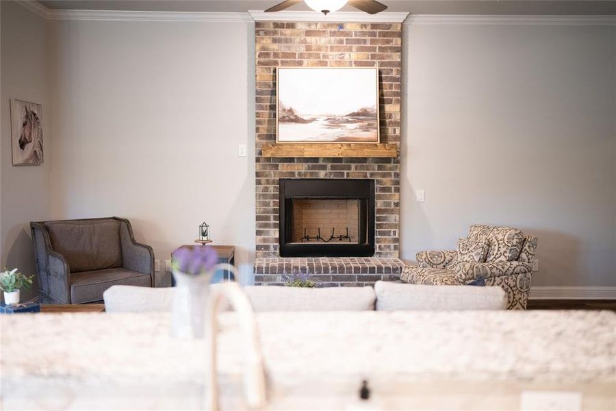 Living room with ceiling fan, crown molding, hardwood / wood-style flooring, a brick fireplace, and brick wall