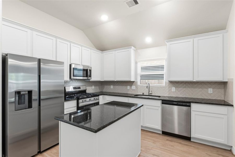Modern kitchen with stainless steel appliances, white cabinets, and a black granite countertop island. Bright and spacious with a stylish backsplash and ample storage.