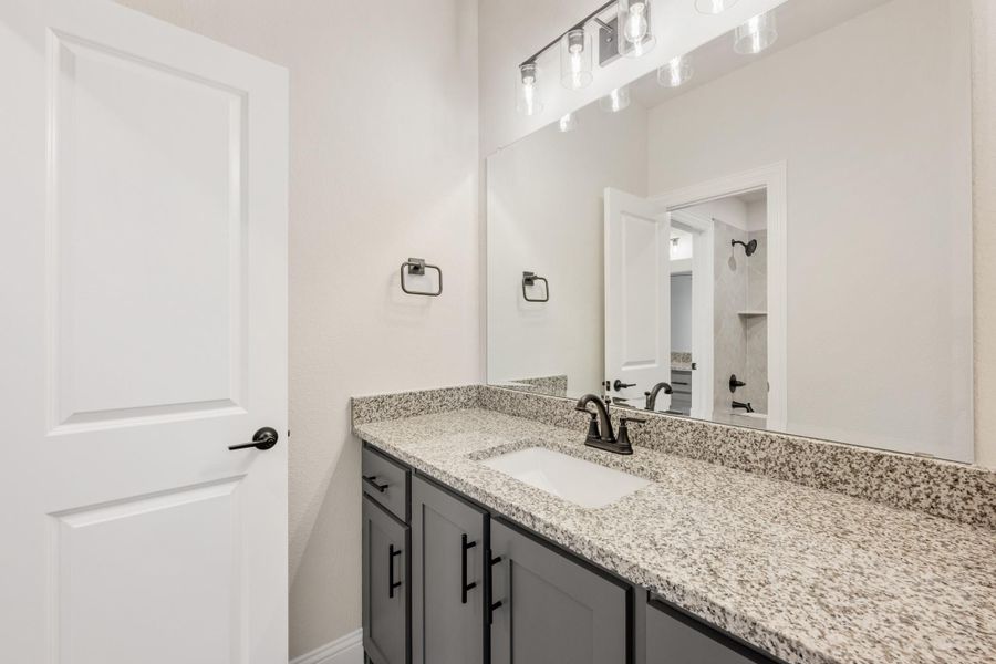 Bathroom vanity with granite countertop, gray cabinets, single sink, and large mirror with overhead lighting
