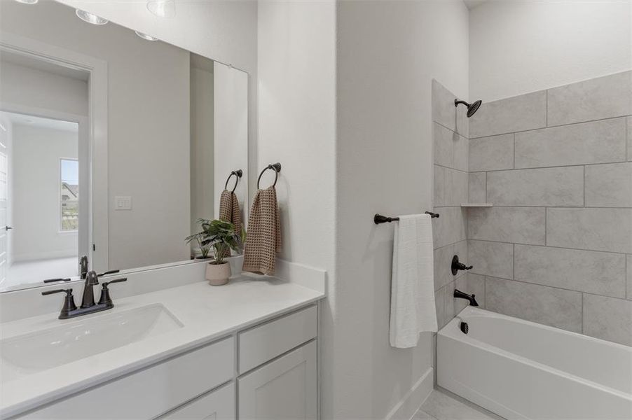 Bathroom featuring a single vanity with a white countertop and integrated sink, matte black faucet, and a shower-tub combination with light grey tile surround