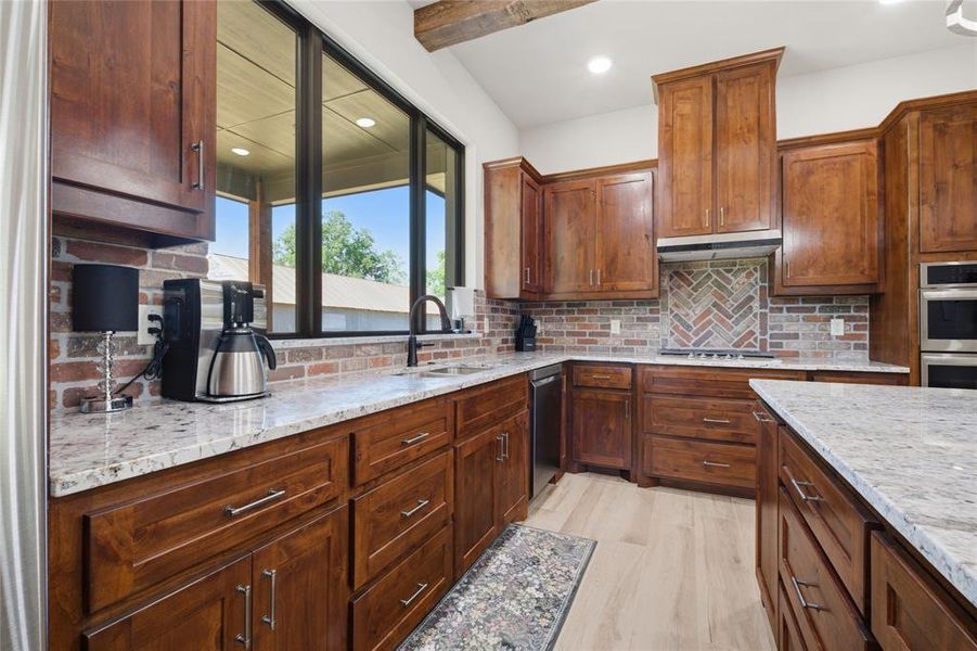 Kitchen featuring warm wood cabinetry, light granite countertops, stainless steel appliances, a herringbone brick-patterned backsplash, and wood-finish flooring
