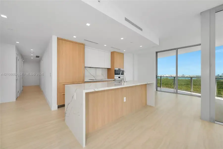 Kitchen featuring wood-finish cabinetry, stone-surfaced waterfall island, integrated appliances, recessed lighting, and floor-to-ceiling glass sliding doors