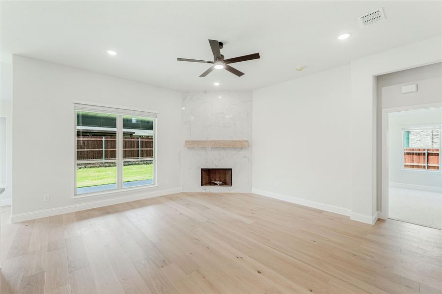 Open living room with light hardwood floors, marble fireplace, and ceiling fan