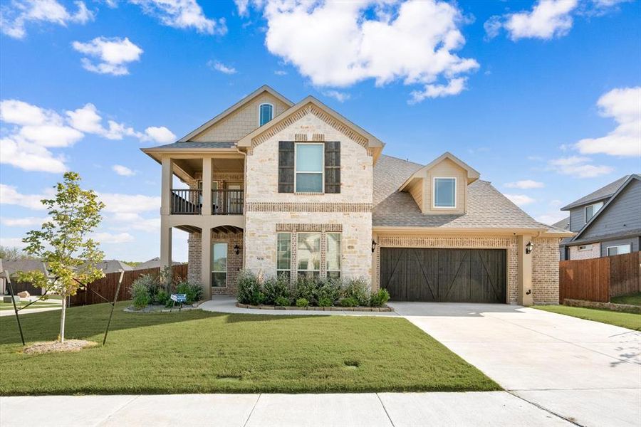 Brick & stone elevation with a covered porch & upstairs balcony, and stained wood garage door.