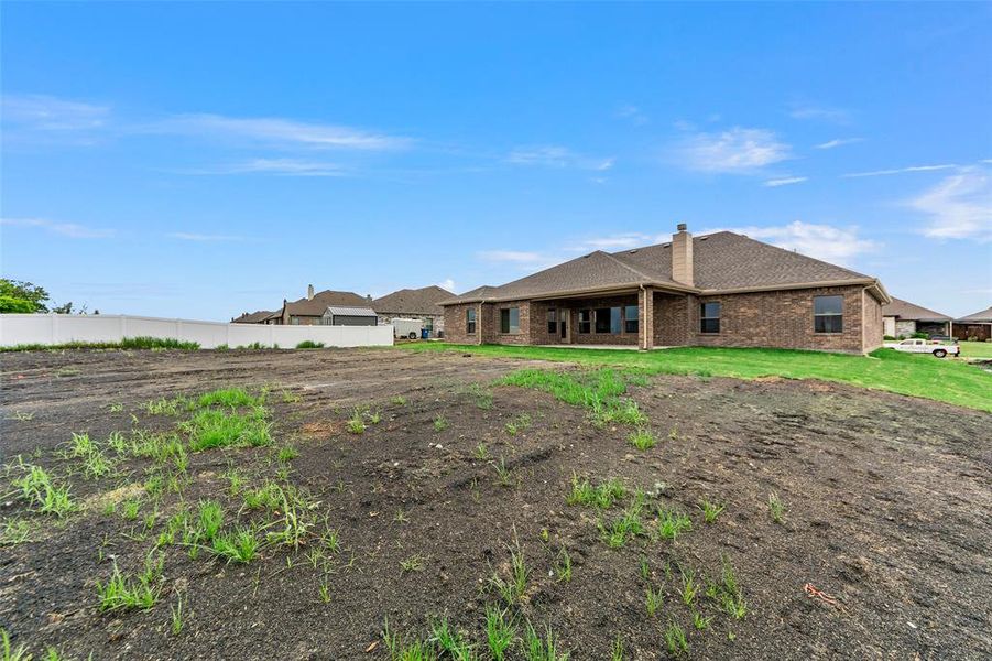 Back of house with brick siding, a chimney, roof with shingles, and fence
