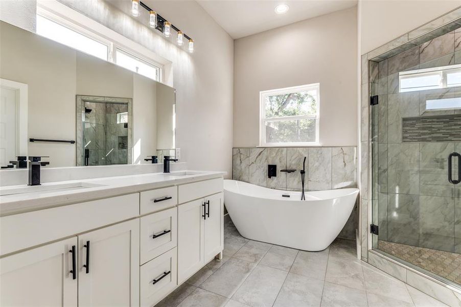 Full bathroom featuring a stall shower, a freestanding tub, double vanity, tile walls, and wainscoting
