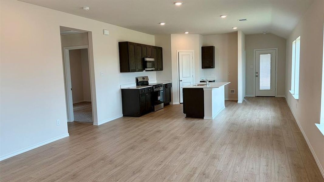 Open-concept kitchen and living area featuring wood-finish flooring, dark wood cabinetry, white countertops, and stainless steel appliances