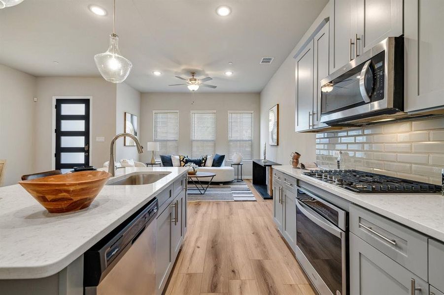 Kitchen with sink, a center island with sink, stainless steel appliances, light stone countertops, and light hardwood / wood-style floors