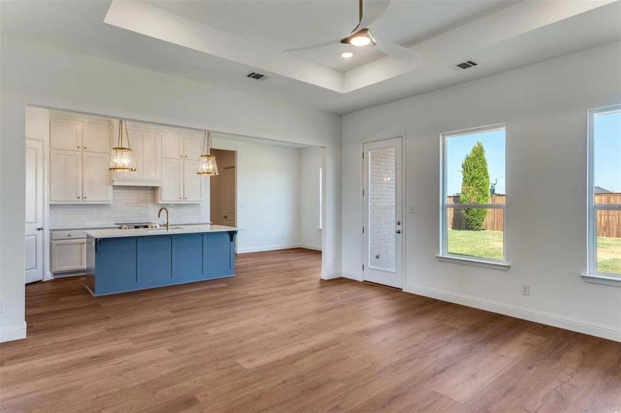 Kitchen featuring a raised ceiling, tasteful backsplash, light wood finished floors, a kitchen island with sink, and ceiling fan Kitchen featuring a raised ceiling, tasteful backsplash, light wood finished floors, a kitchen island with sink, and ceiling fan