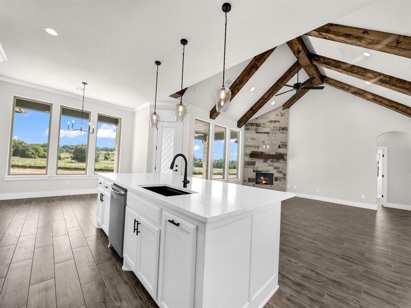 Kitchen featuring beamed ceiling, white cabinetry, pendant lighting, a center island with sink, and a large fireplace