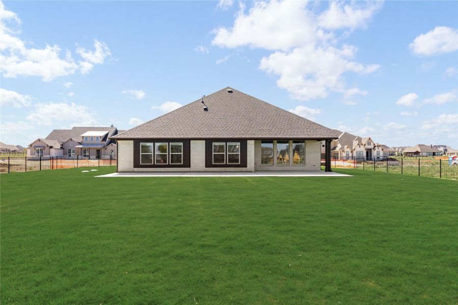 Rear view of single-story brick home with hip roof, covered patio, and large fenced backyard