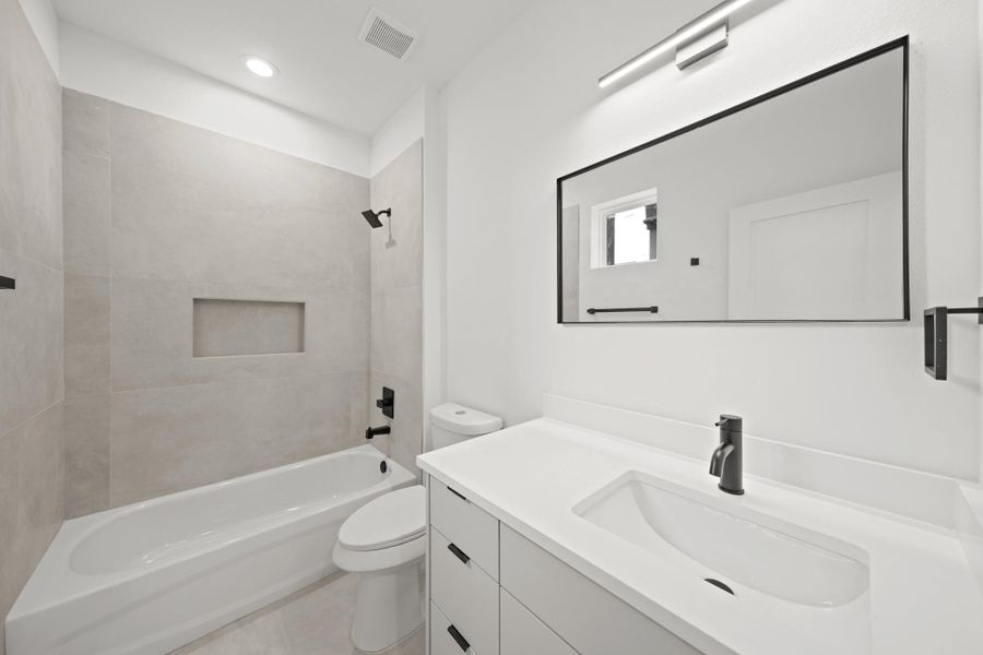 Serving as the home's third full bath, this ensuite bath includes a Quartz counter, large black-framed mirror, recessed lighting and a tile surrounded tub/shower combo with shampoo niche. Serving as the home's third full bath, this ensuite bath includes a Quartz counter, large black-framed mirror, recessed lighting and a tile surrounded tub/shower combo with shampoo niche.