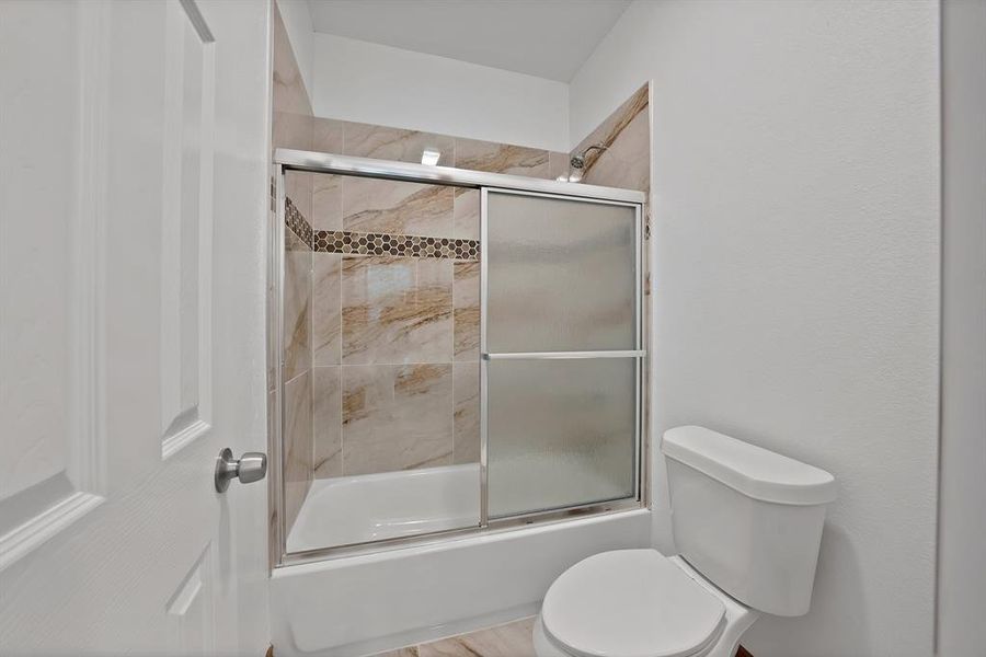 Full bathroom with combined bath / shower with glass door and toilet