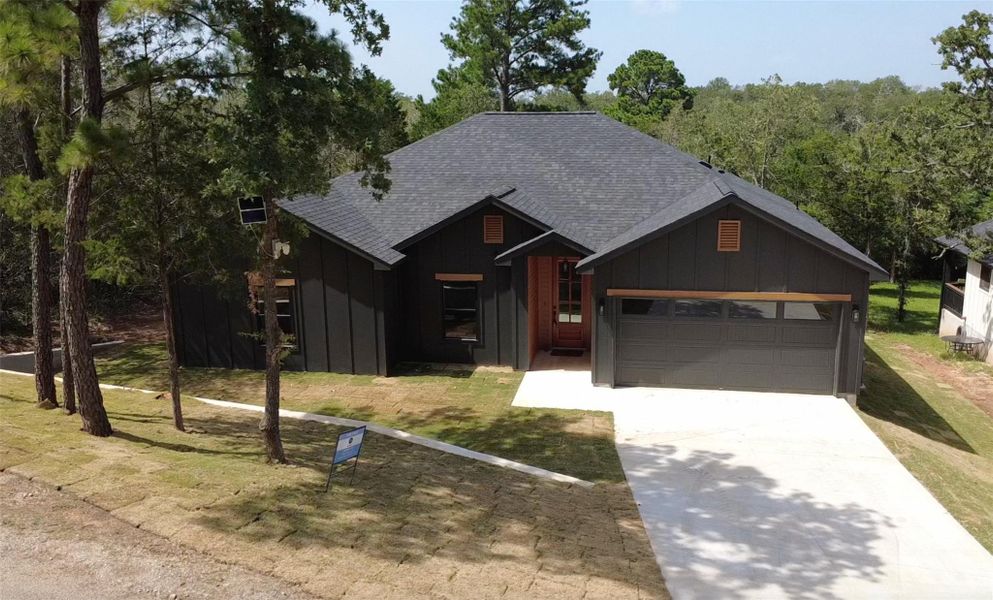 A new construction home with dark siding and a matching garage sits amidst a wooded landscape. A new construction home with dark siding and a matching garage sits amidst a wooded landscape.